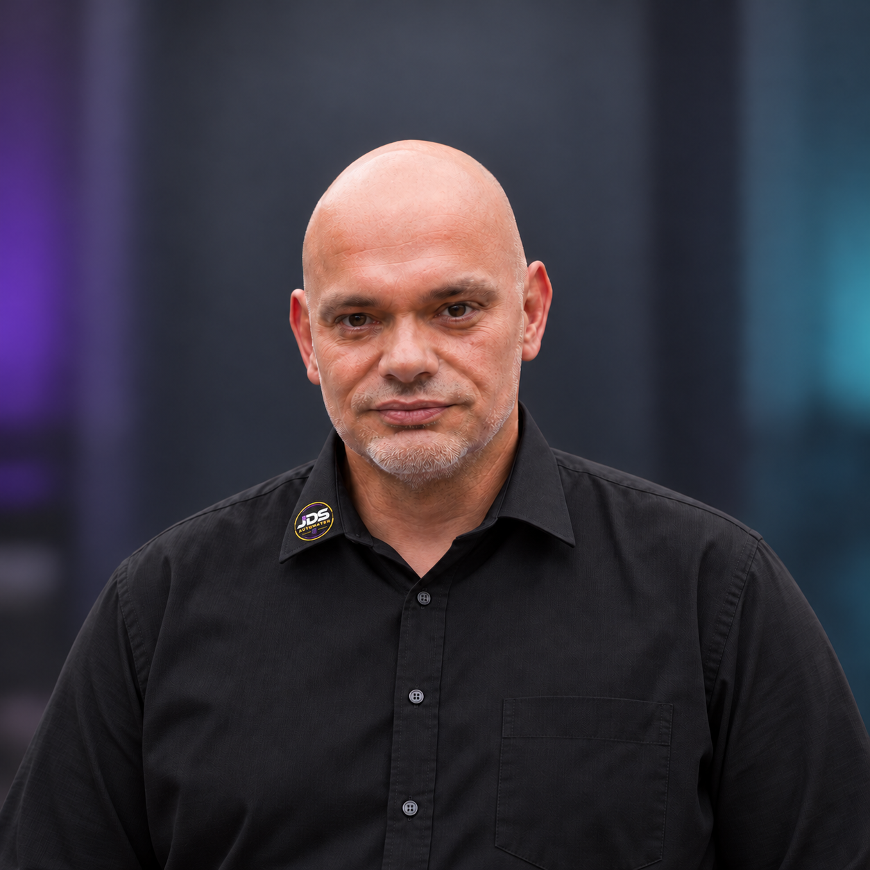 Daniel Kindl im schwarzen Hemd mit JDS-Logo am Kragen vor anthrazitfarbenem Hintergrund